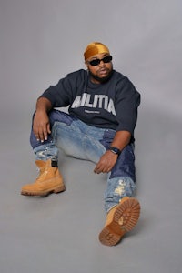 a man sitting on the ground wearing a hat and jeans